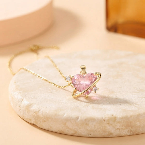 Close-up of a gold-tone necklace with a pink crystal centerpiece inside an orbital ring on a cream stone surface.
