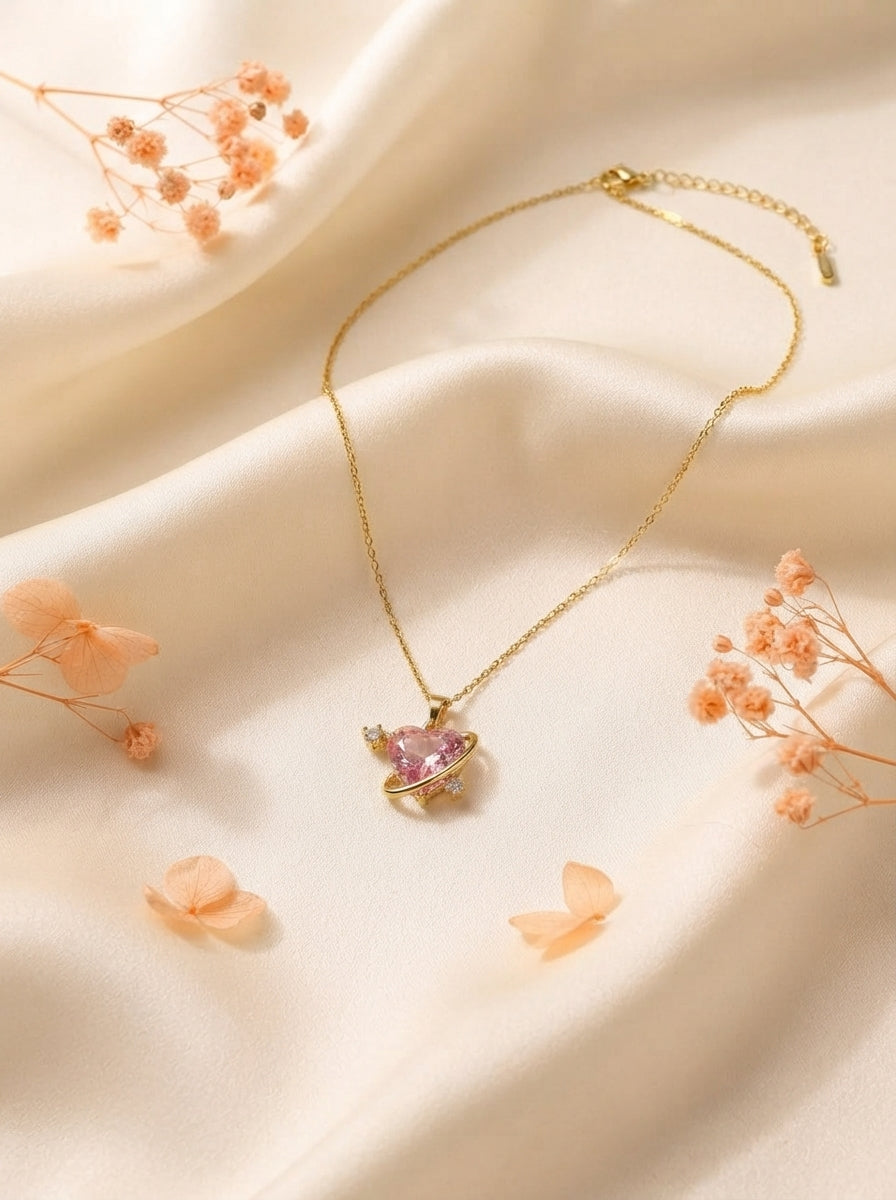 Celestial Pink Orbit Necklace with a pink crystal and gold orbital ring displayed on cream silk with peach floral accents.